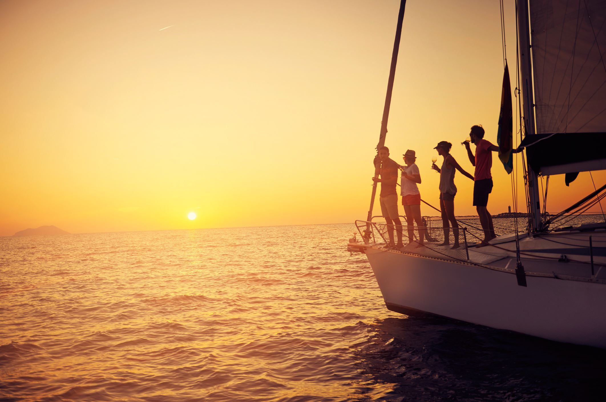 People standing on a sailboat in the water, the sunsetting in the background